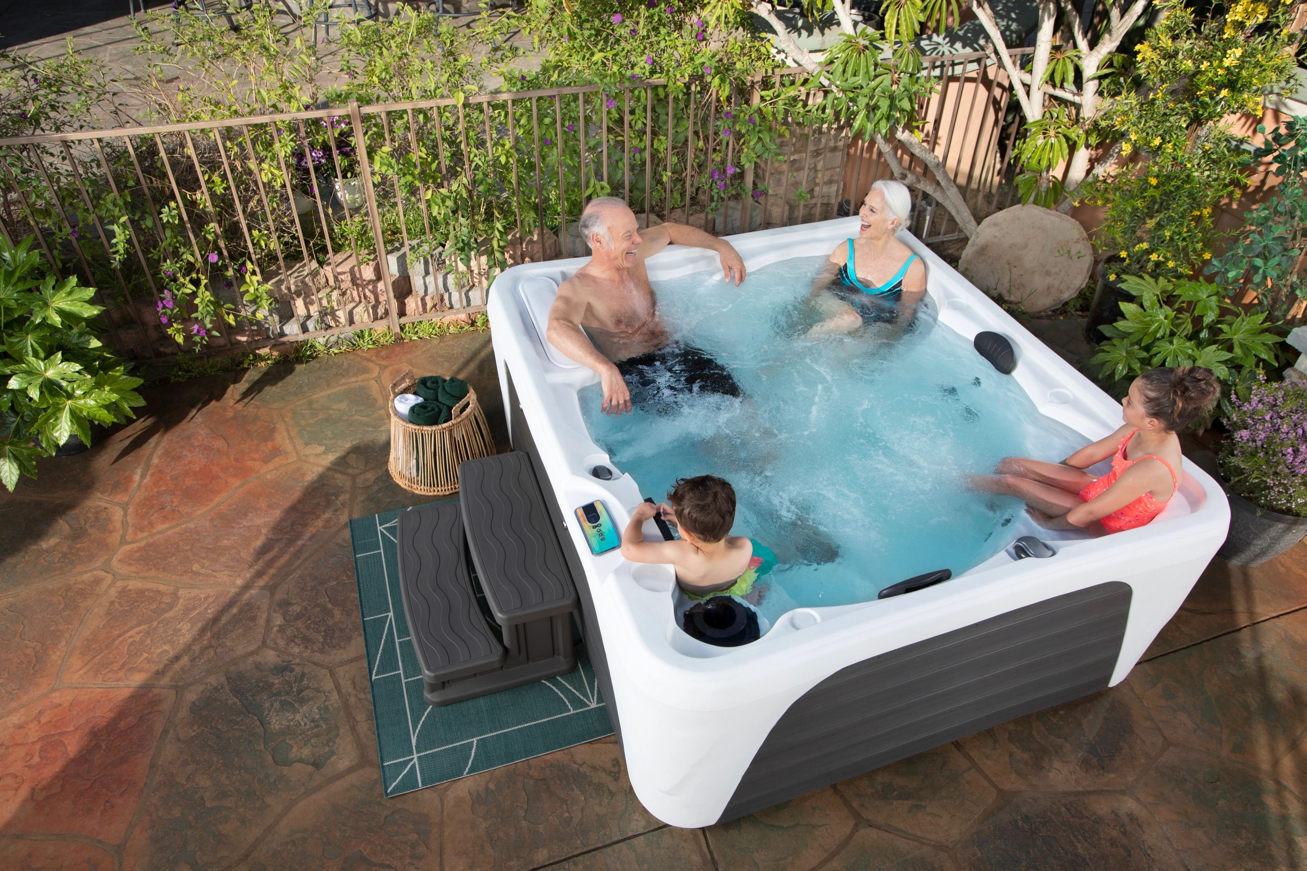 family enjoying a soak in a fantasy entice 5 person plug n play hot tub in their backyard on a paver patio