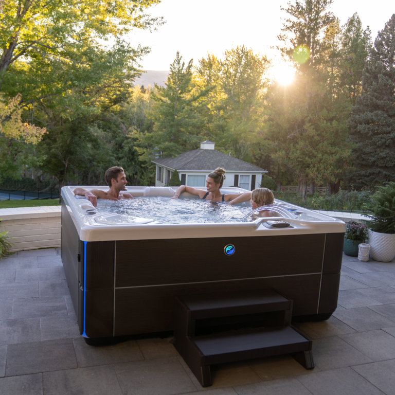 family in a salt water hot tub in their backyard with with sun setting behind the trees.